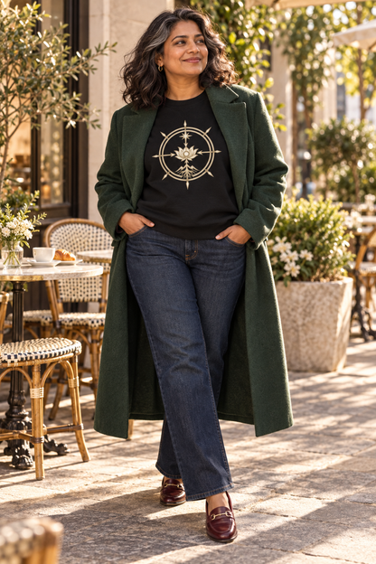 Woman wearing the black Aligned Abundance Seal sweatshirt with tailored navy wide-leg trousers and burgundy shoes in an elegant outdoor café setting.